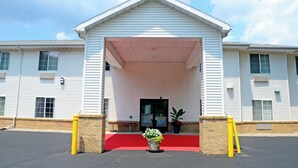 A building with a covered entrance, a red carpet, and potted plants. - Budget Host Inn (Allegan)