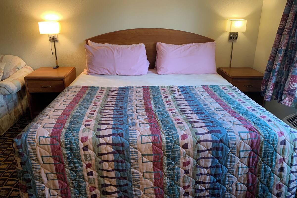 Une chambre d’hôtel avec un grand lit, deux tables de chevet, une petite table d’appoint, une couvre-lit à motifs et deux lampes fixées au mur.