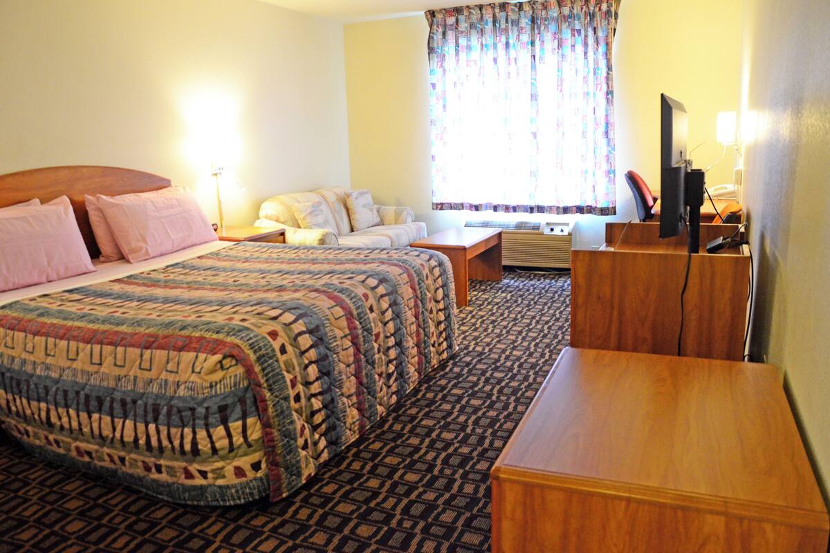 Une chambre d’hôtel avec un grand lit, un bureau, une chaise, une télévision et une fenêtre avec des rideaux.
