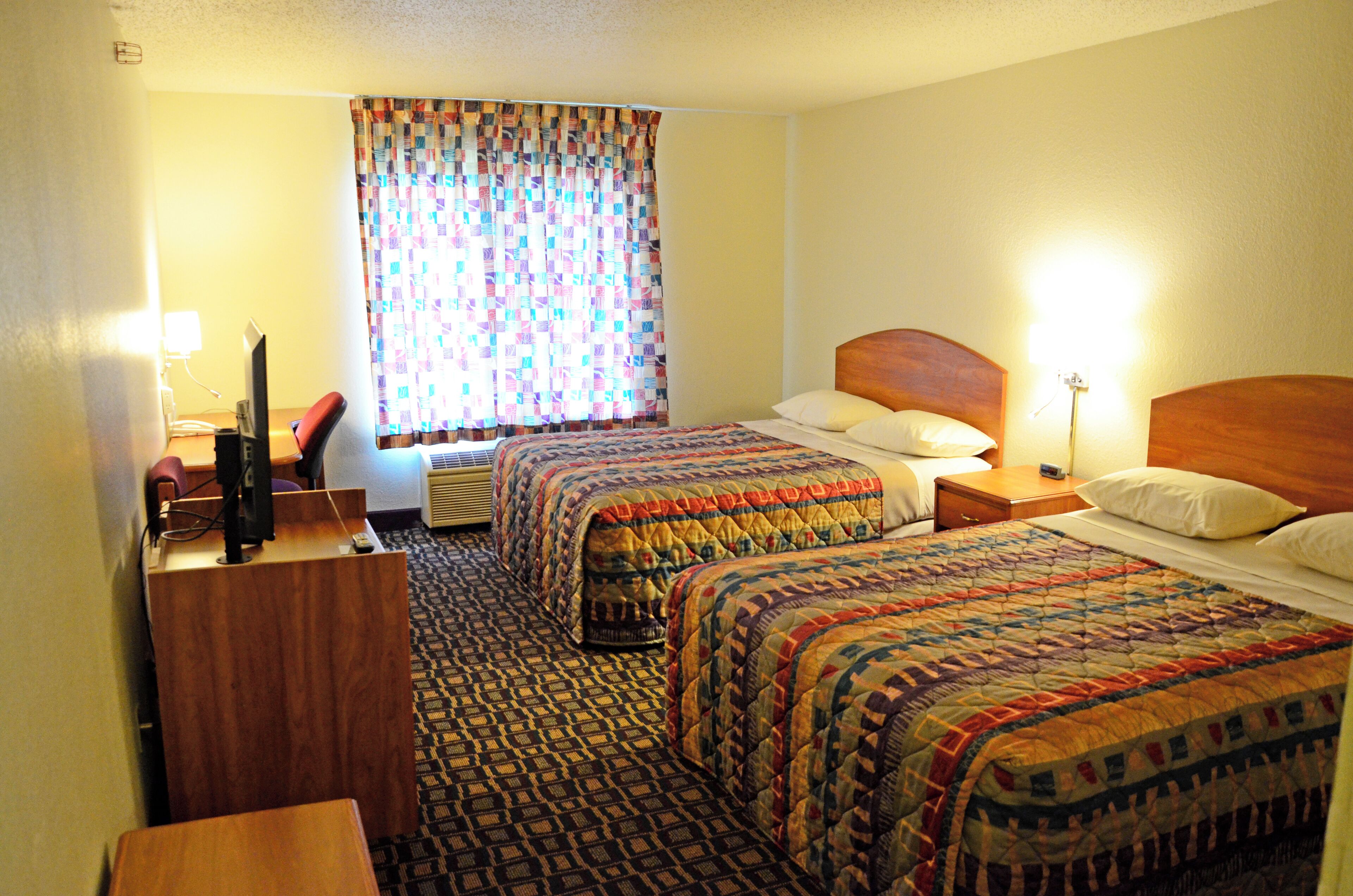 A hotel room with two beds, a desk, a chair, a television, and a window with curtains.