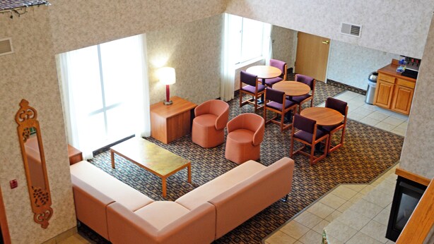 A hotel room with a sofa, chairs, a small table, a lamp, and a kitchen area. - Budget Host Inn (Allegan)