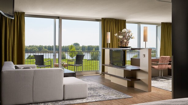 A modern hotel room with a large balcony, a sofa, a TV, and a dining area. - Van der Valk Hotel ARA (Zwijndrecht)