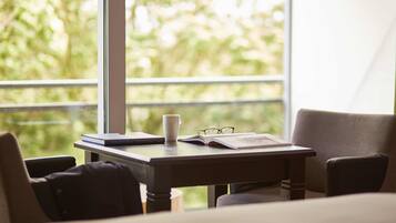 A room with a large window, a desk with a book, a cup, and glasses.