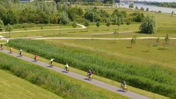 Une piste cyclable asphaltée, bordée de champs verdoyants et d’arbres, avec une rivière en arrière-plan, où l’on peut voir des cyclistes.