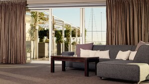 A modern living room with a grey sofa, a wooden coffee table, and a vase with a single flower. - Van der Valk Hotel ARA (Zwijndrecht)