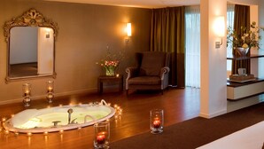 A hotel room with a large bathtub, a chair, a bedside table with a vase of flowers, and a bed. - Van der Valk Hotel ARA (Zwijndrecht)