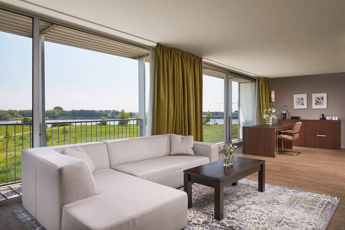 A modern living room with a sofa, a coffee table, and a view of a lake through large windows.