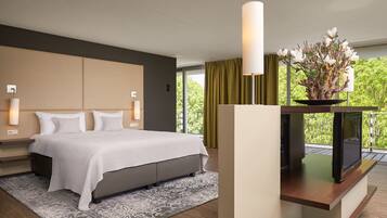 A modern hotel room with a large bed, bedside lamps, a flat-screen TV, and a balcony with a view of greenery.