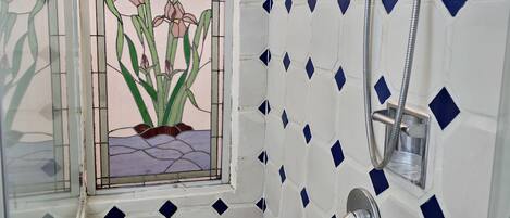 A bathroom with a shower, a window with a stained glass design, and a tiled wall with a geometric pattern.