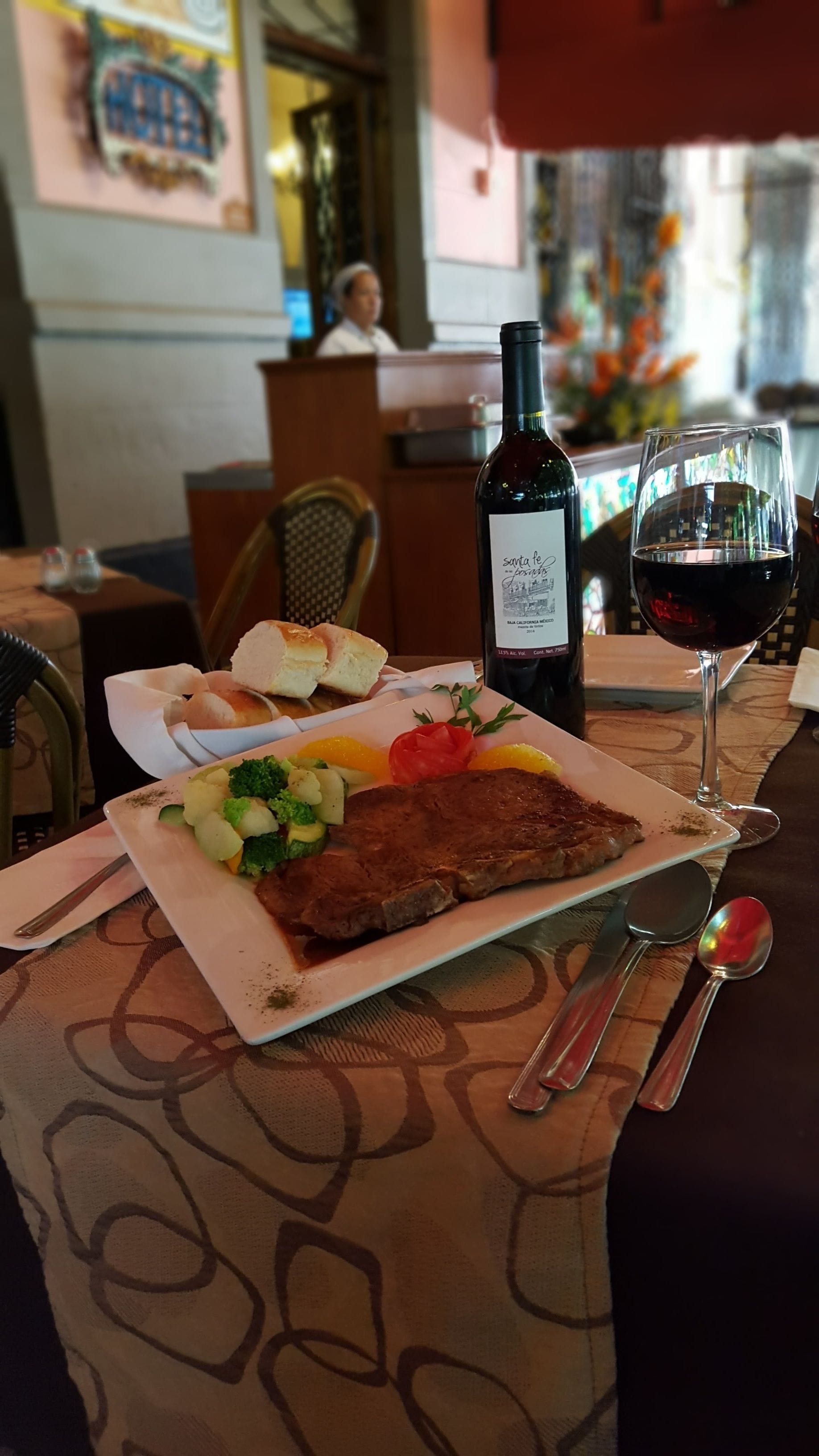 A dining table with a plate of food, a bottle of wine, and a glass of red wine.