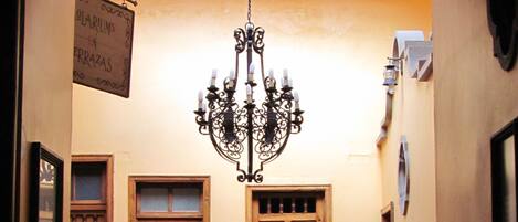 Un pasillo con candelabro, puertas de madera y una escalera con barandillas de metal.