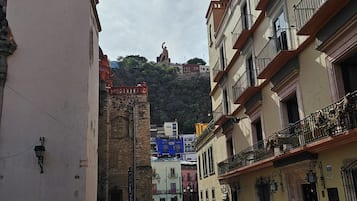 Una calle adoquinada con edificios históricos, una torre de campanas y una estatua en una colina.