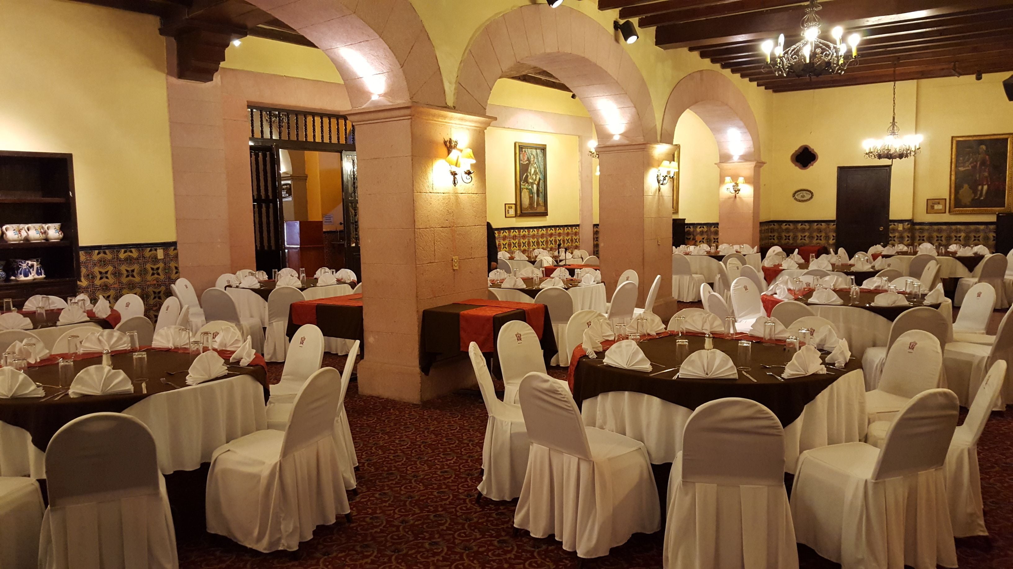 Un salón de banquetes con mesas redondas, sillas blancas y candelabros.