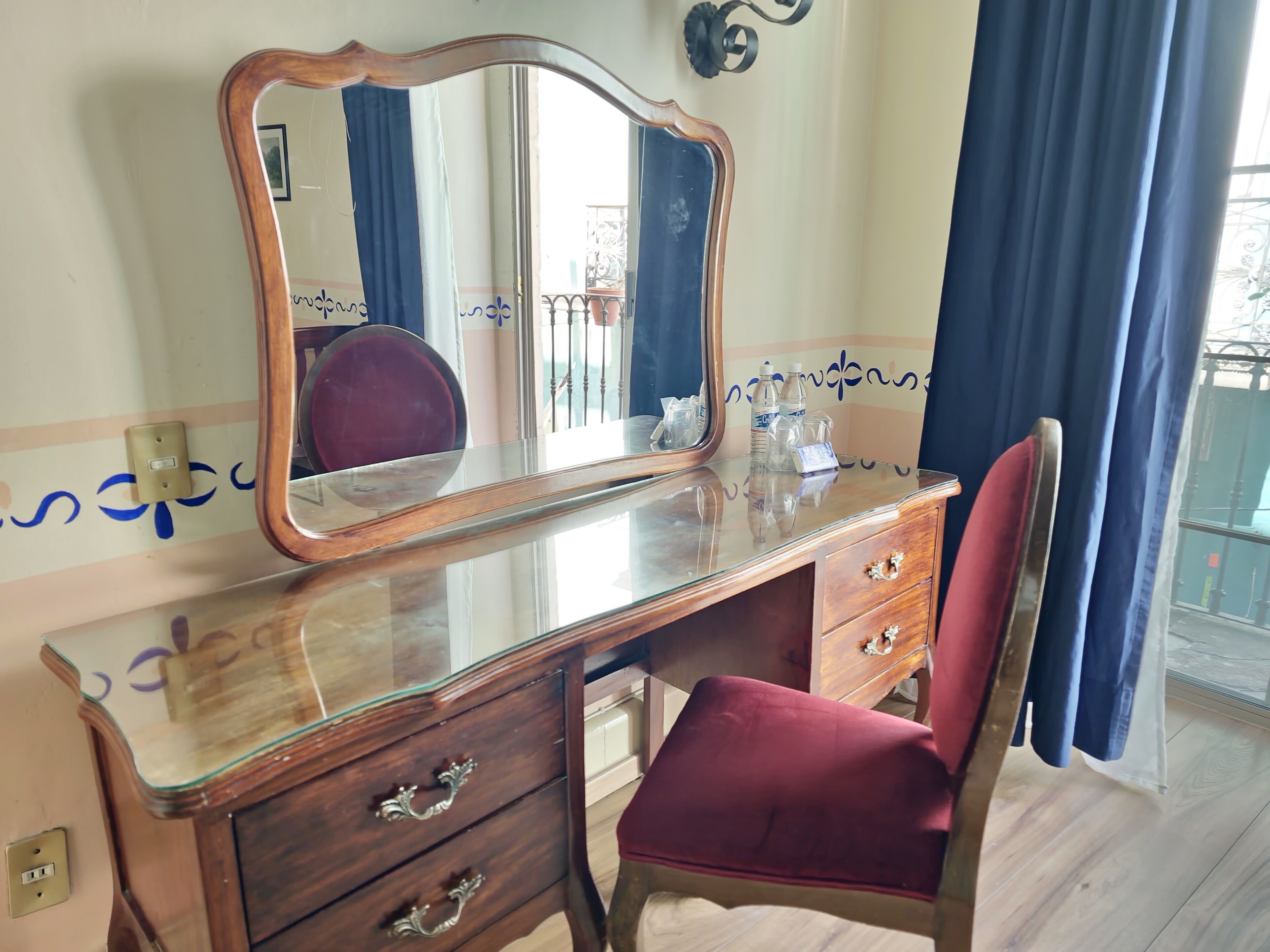 A wooden vanity with a glass top, a mirror, and a red chair.