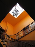 Una escalera con barandales de metal ornamentados y un tragaluz arriba.