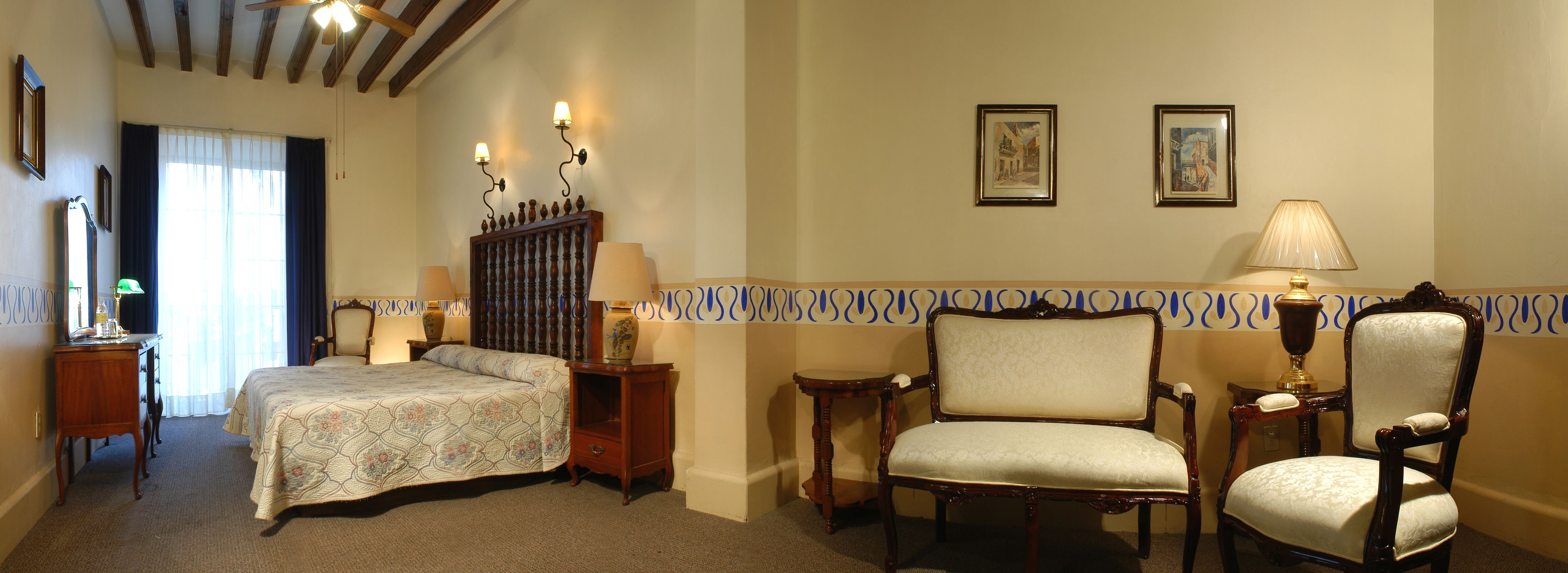 Ein Hotelzimmer mit einem Bett, zwei Stühlen, einem Nachttisch, einem Spiegel und zwei Wandleuchten.