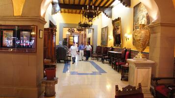 A hotel lobby with a central corridor, wooden furniture, a large vase, and a chandelier.