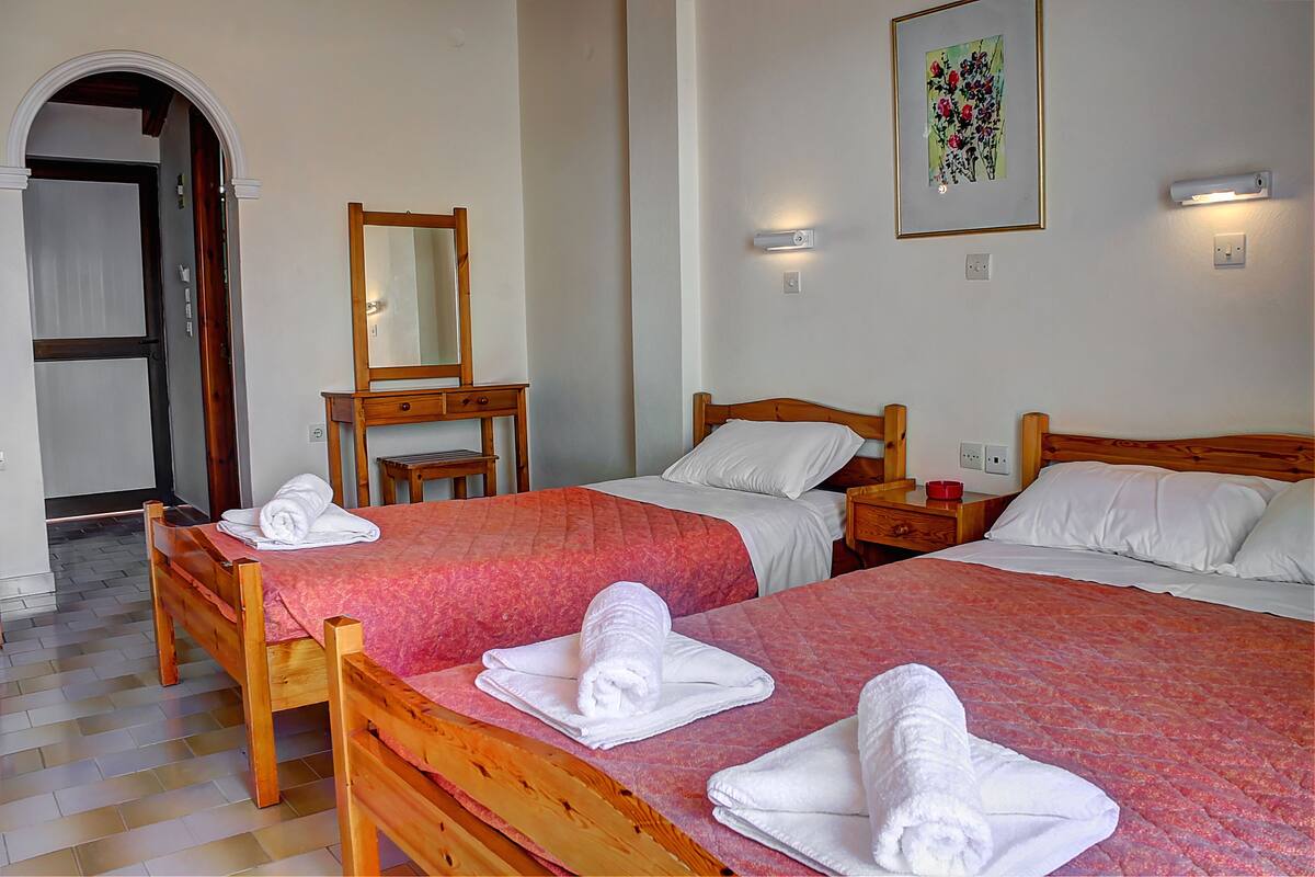 A hotel room with two wooden beds, each with a pink quilt and white linens, a wooden nightstand, a mirror, and a framed floral artwork on the wall.