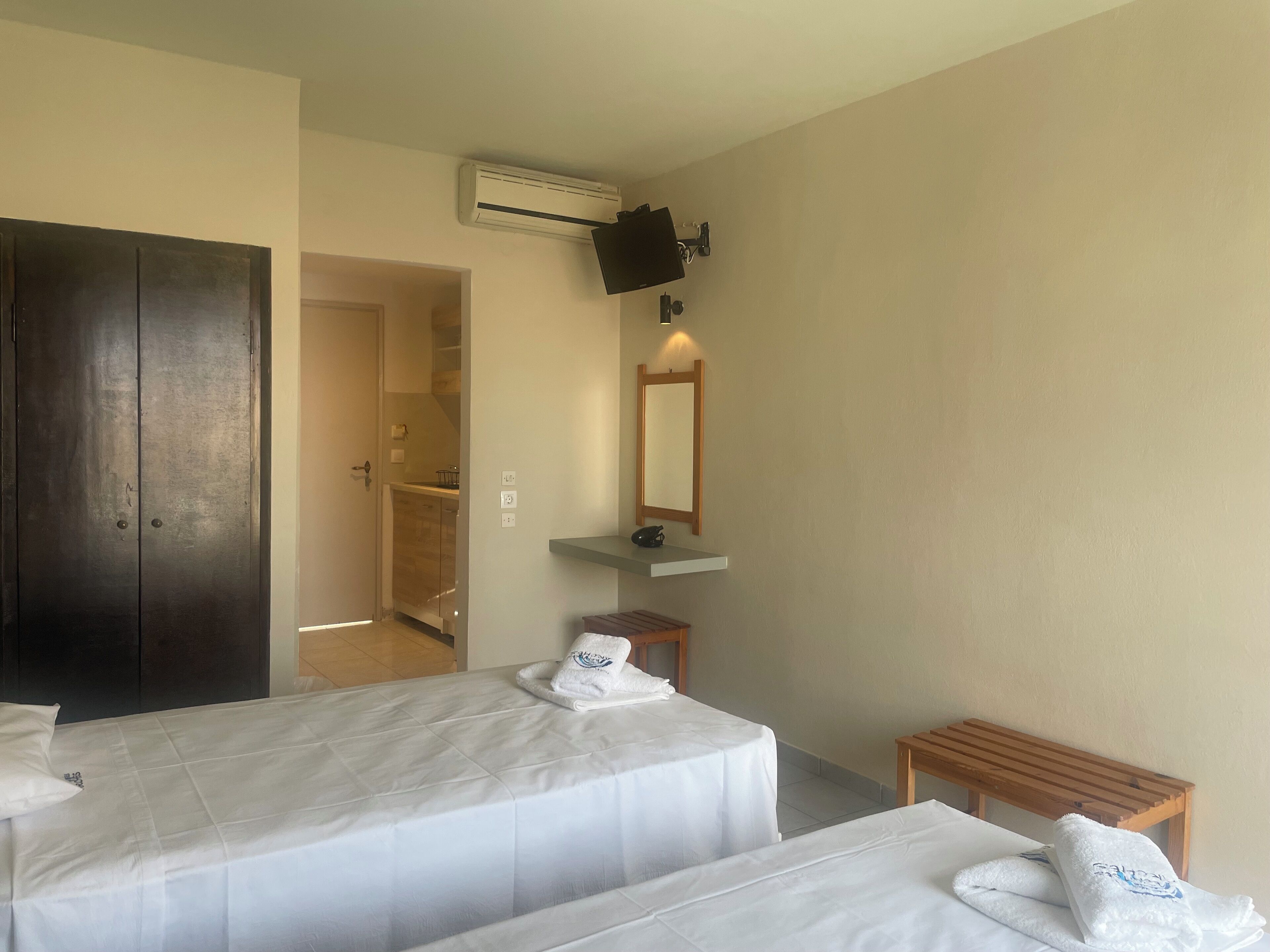 Habitación de hotel con dos camas, un banco de madera, una mesita, un espejo y un equipo de aire acondicionado.