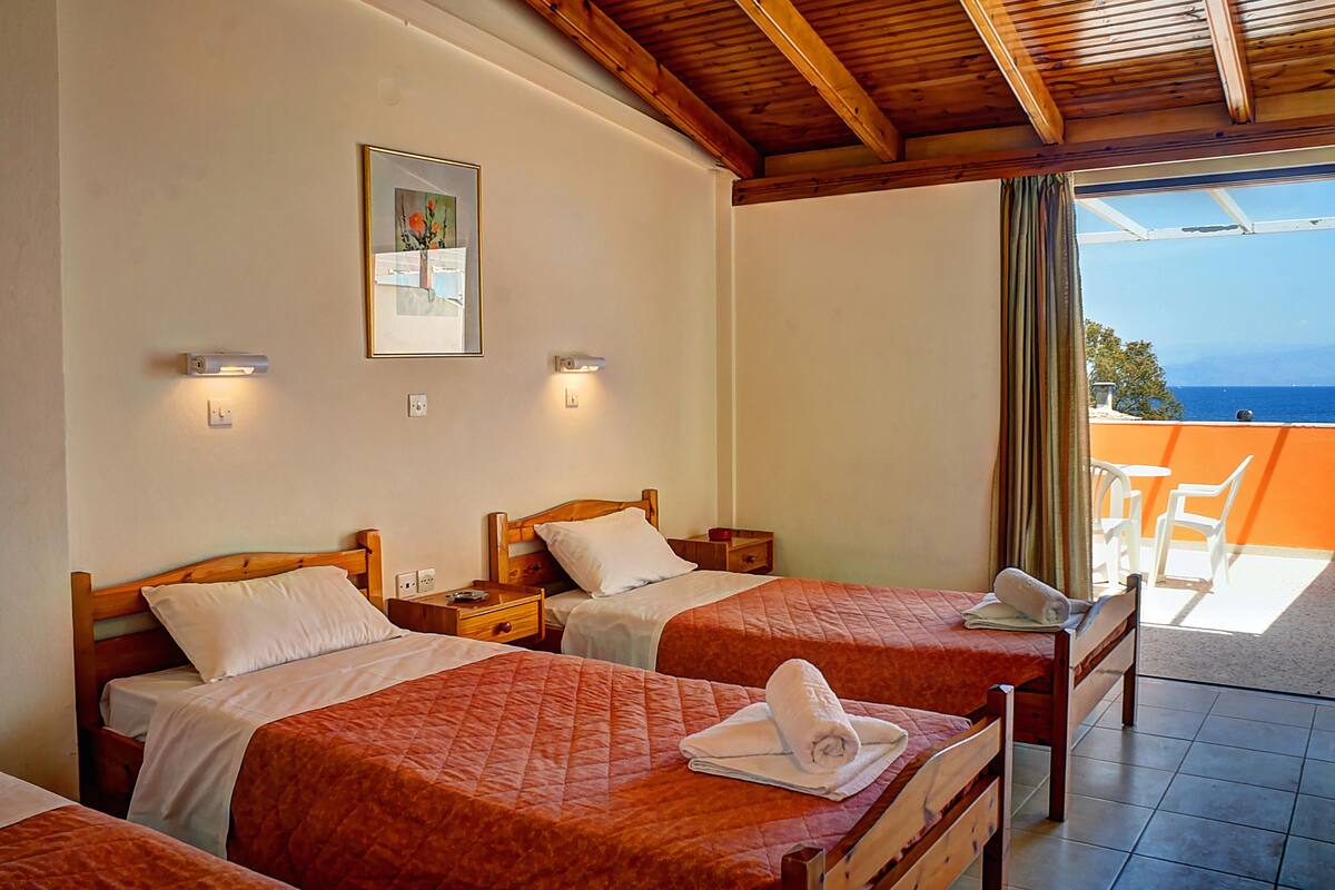 A hotel room with two beds, a painting on the wall, and a view of the sea through a window.