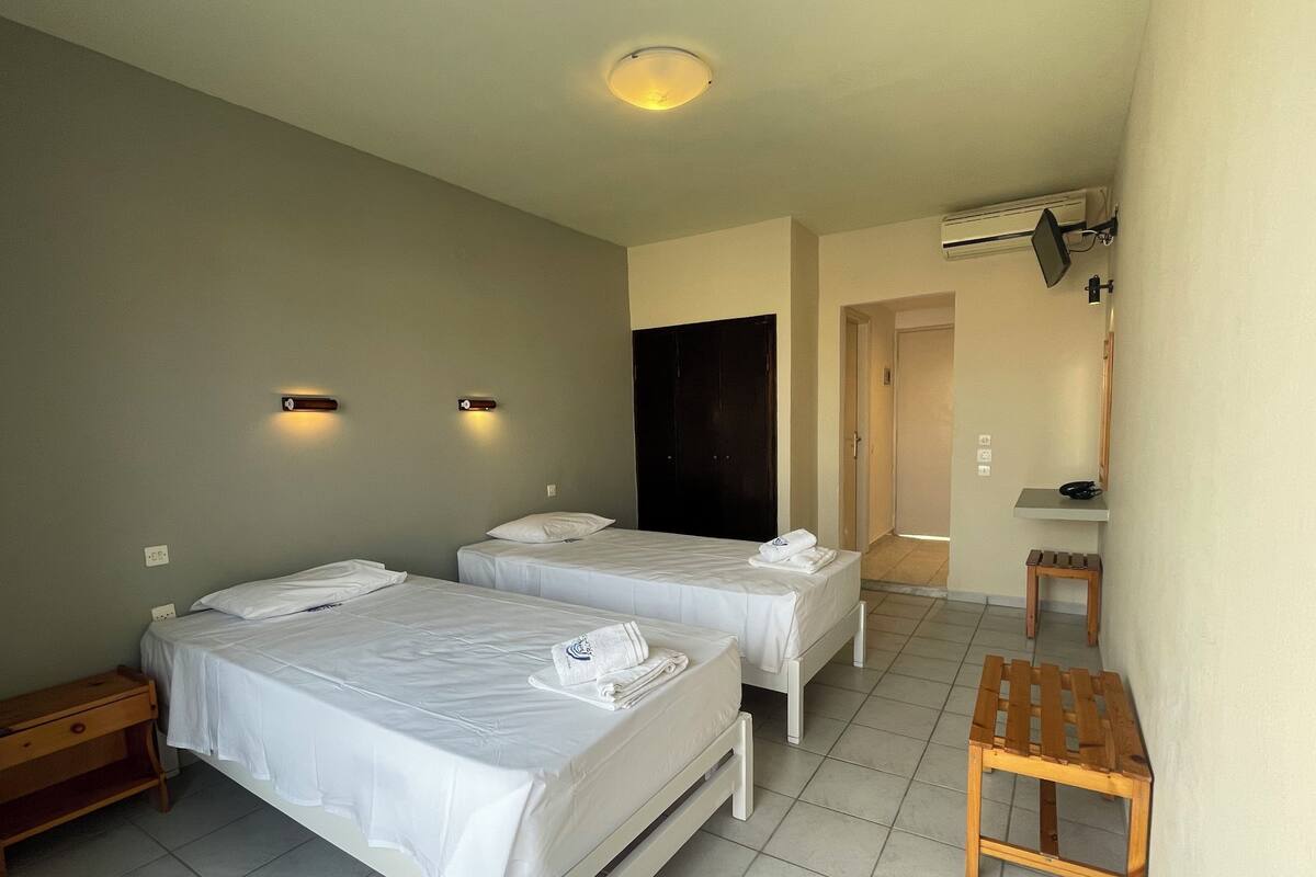 A hotel room with two beds, a wooden bench, a small table, and a bathroom door.