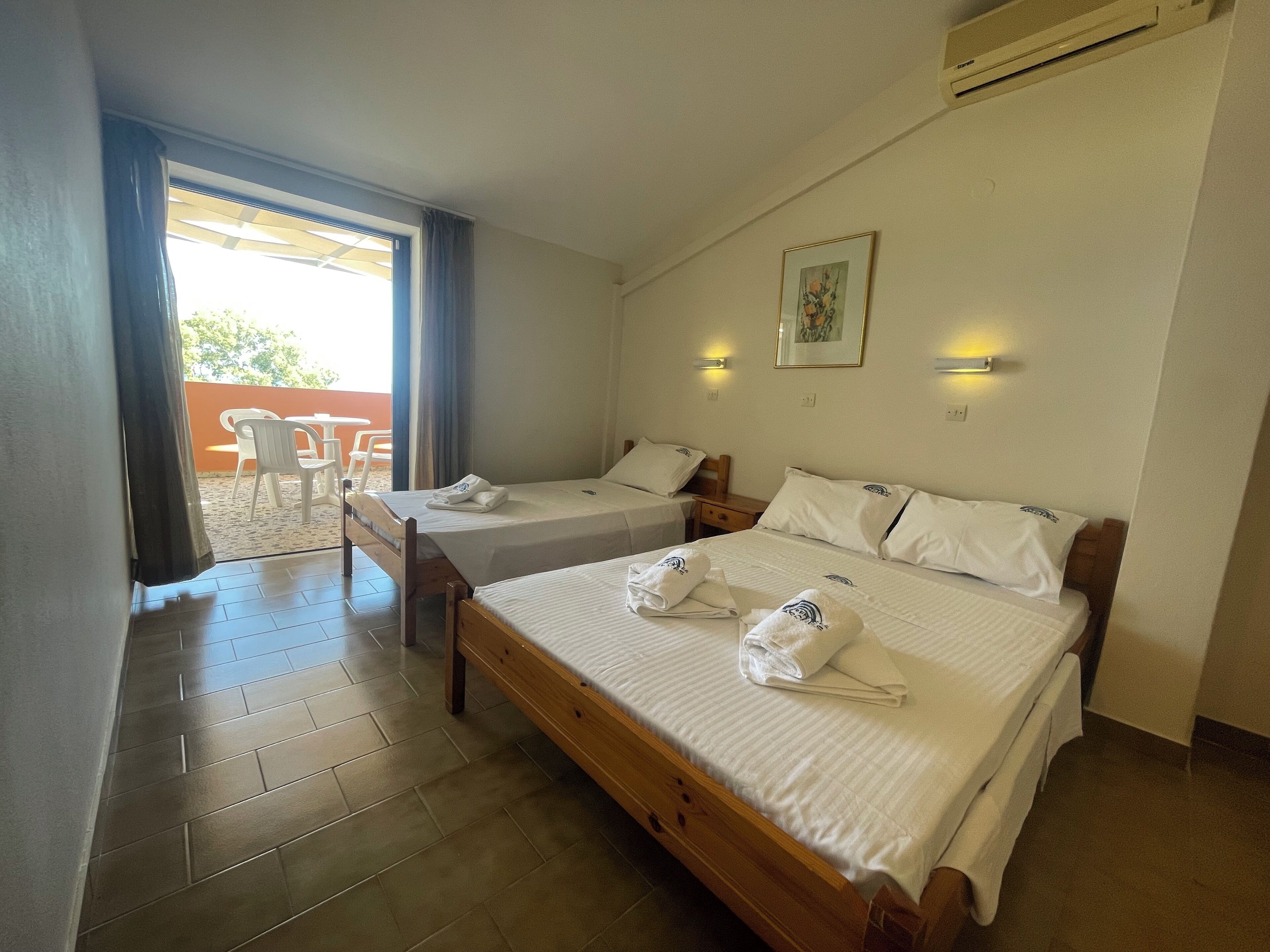 A hotel room with two beds, a small table, and a chair by the window.