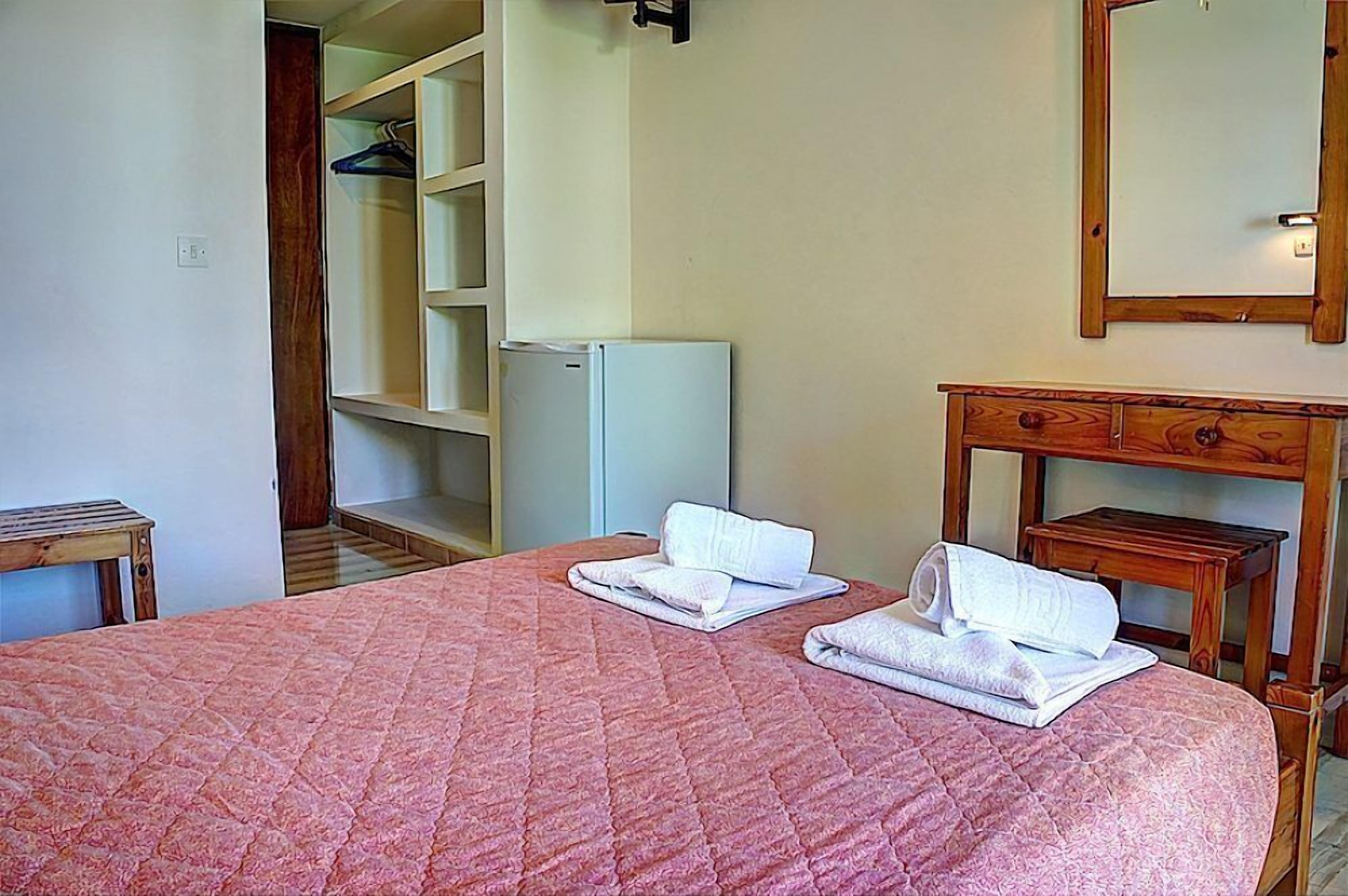 Een hotelkamer met een bed, een houten nachtkastje, een spiegel en een kledingkast.