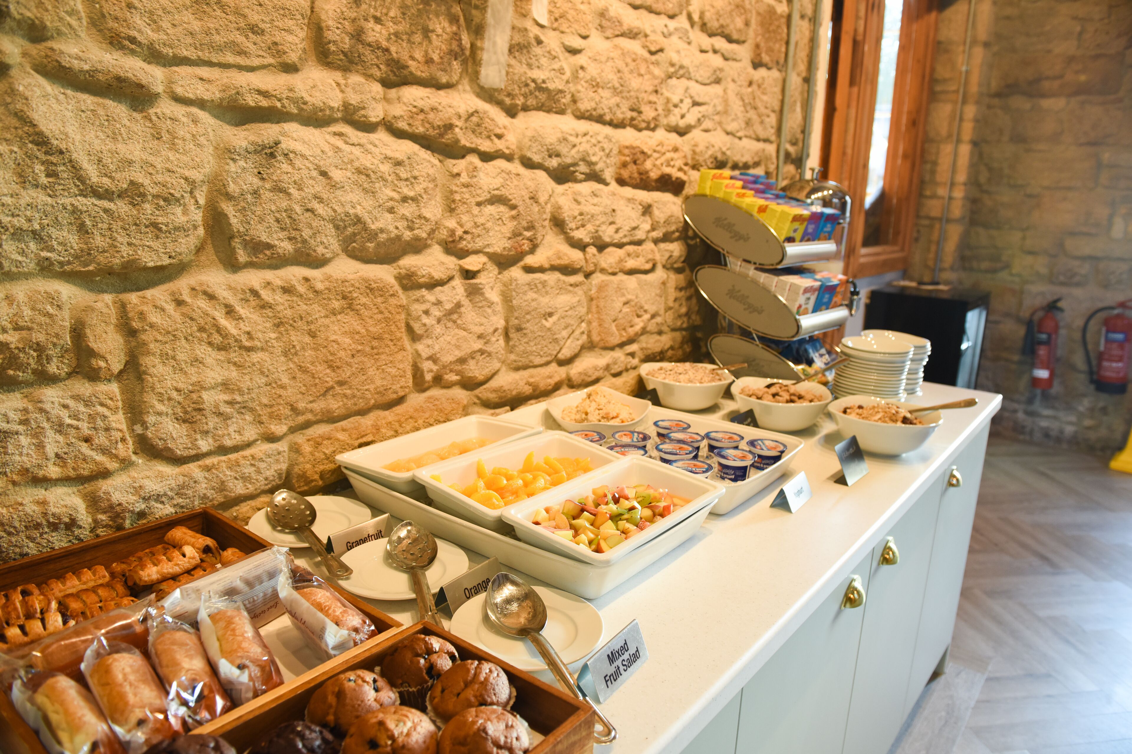 Buffet amb diferents plats i una paret de pedra al fons.