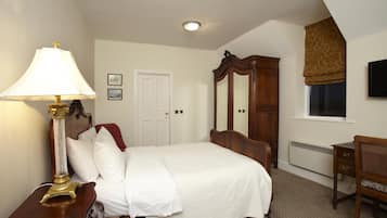Een slaapkamer met een bed, nachtkastje met lamp, dressoir, spiegel, raam met zonwering en een televisie aan de muur.