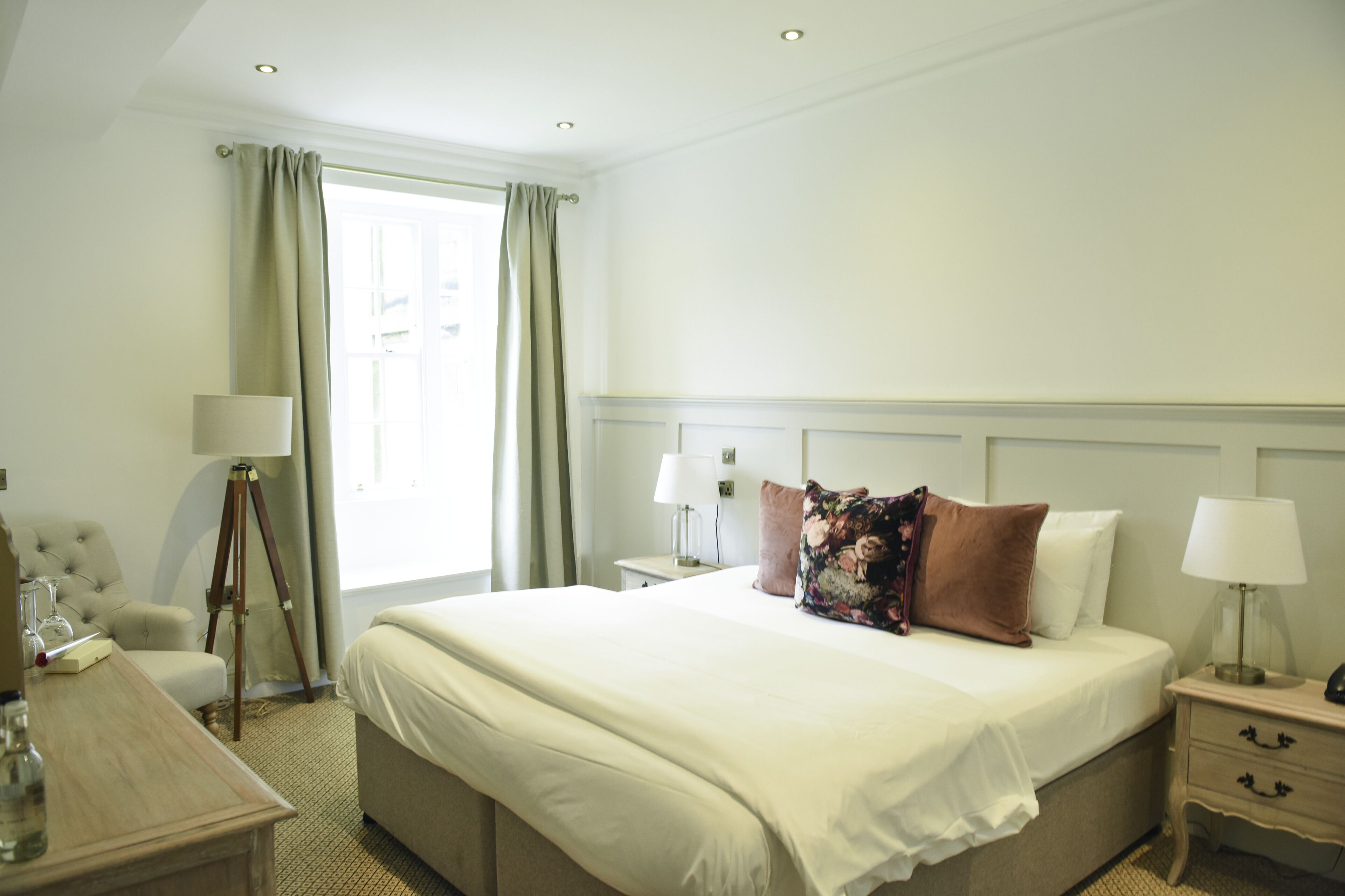 A hotel room with a large bed, bedside tables, a lamp, a chair, and a window with curtains.