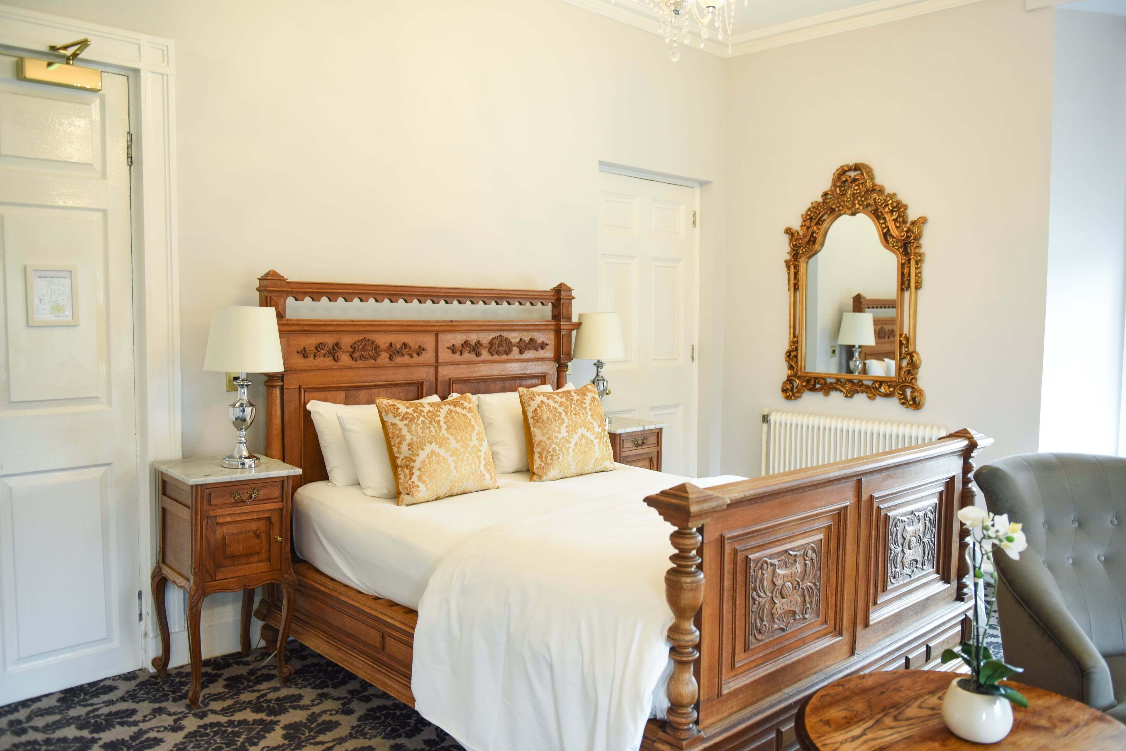 Een keurig opgemaakt slaapkamer met een houten bed, nachtkastjes, een spiegel en een stoel.