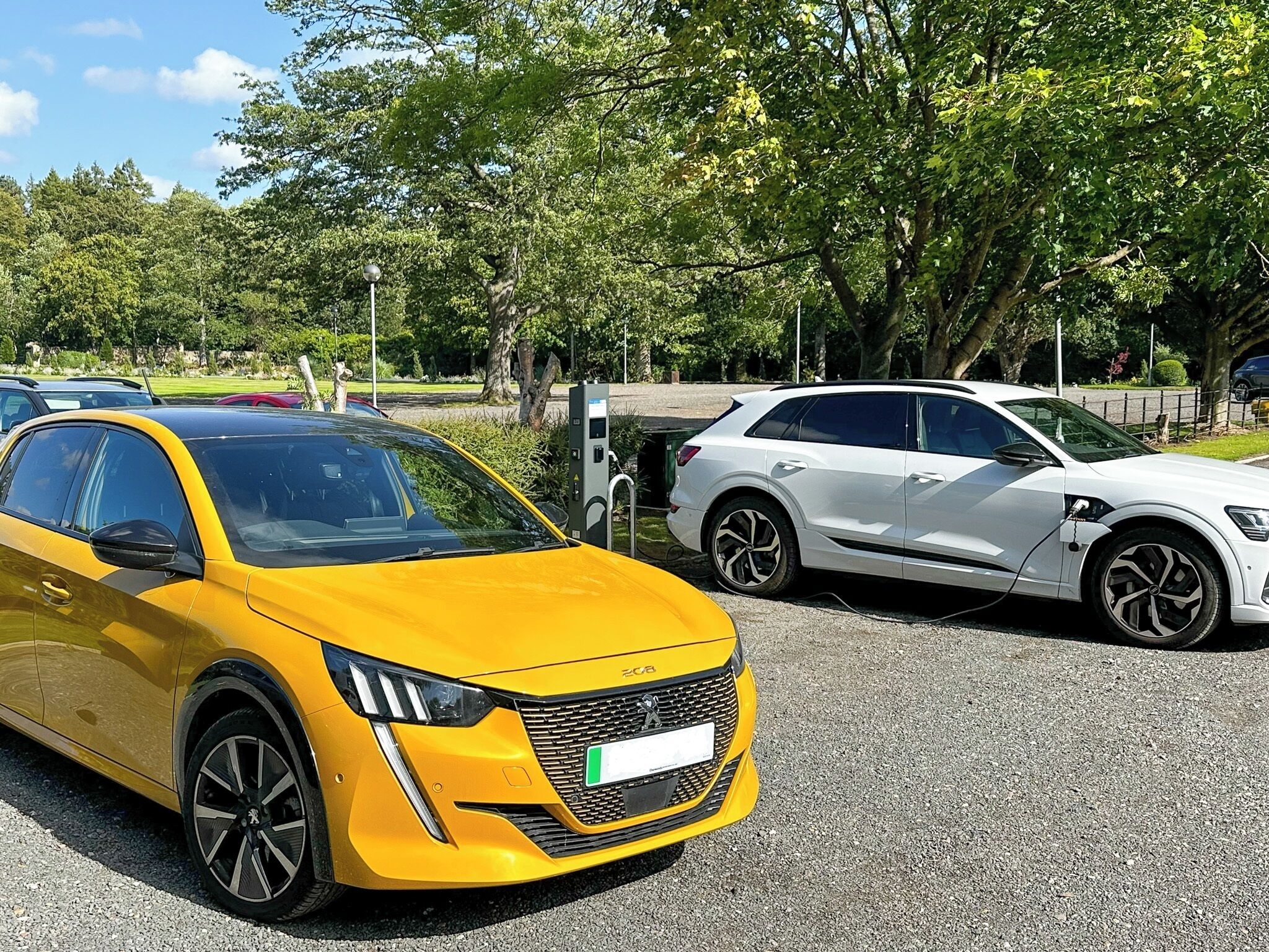 Une voiture jaune est garée à côté d’une voiture blanche sur un parking, avec des arbres en arrière-plan.