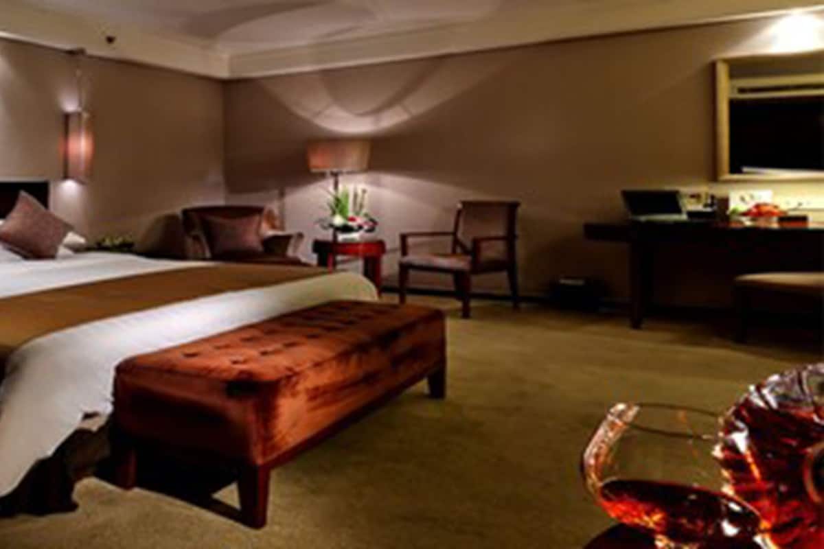 Habitación de hotel con una cama grande, un banco de madera, un escritorio con lámpara y una silla.