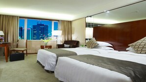 Une chambre d’hôtel avec deux lits, un bureau, une chaise, une télévision et une grande fenêtre donnant sur la ville.