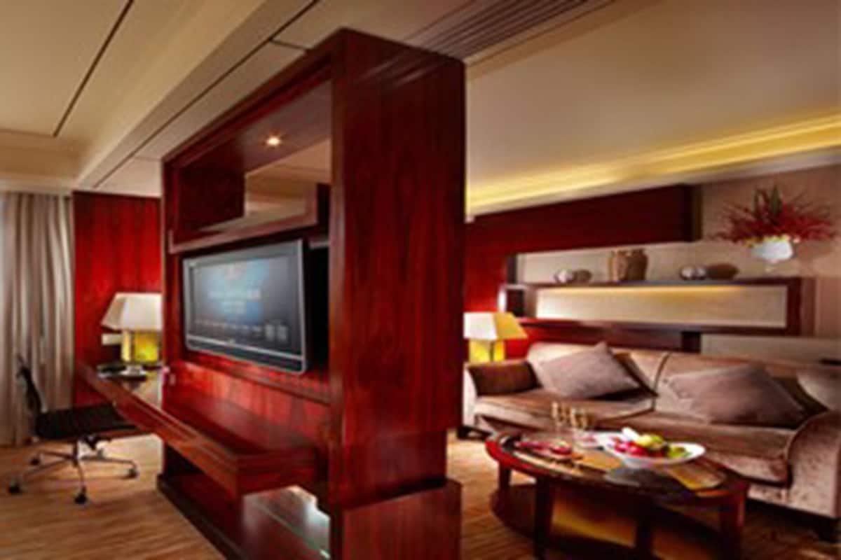 Habitación de hotel con una cama grande, un escritorio con computadora, televisión, sofá y una mesa de comedor con comida.