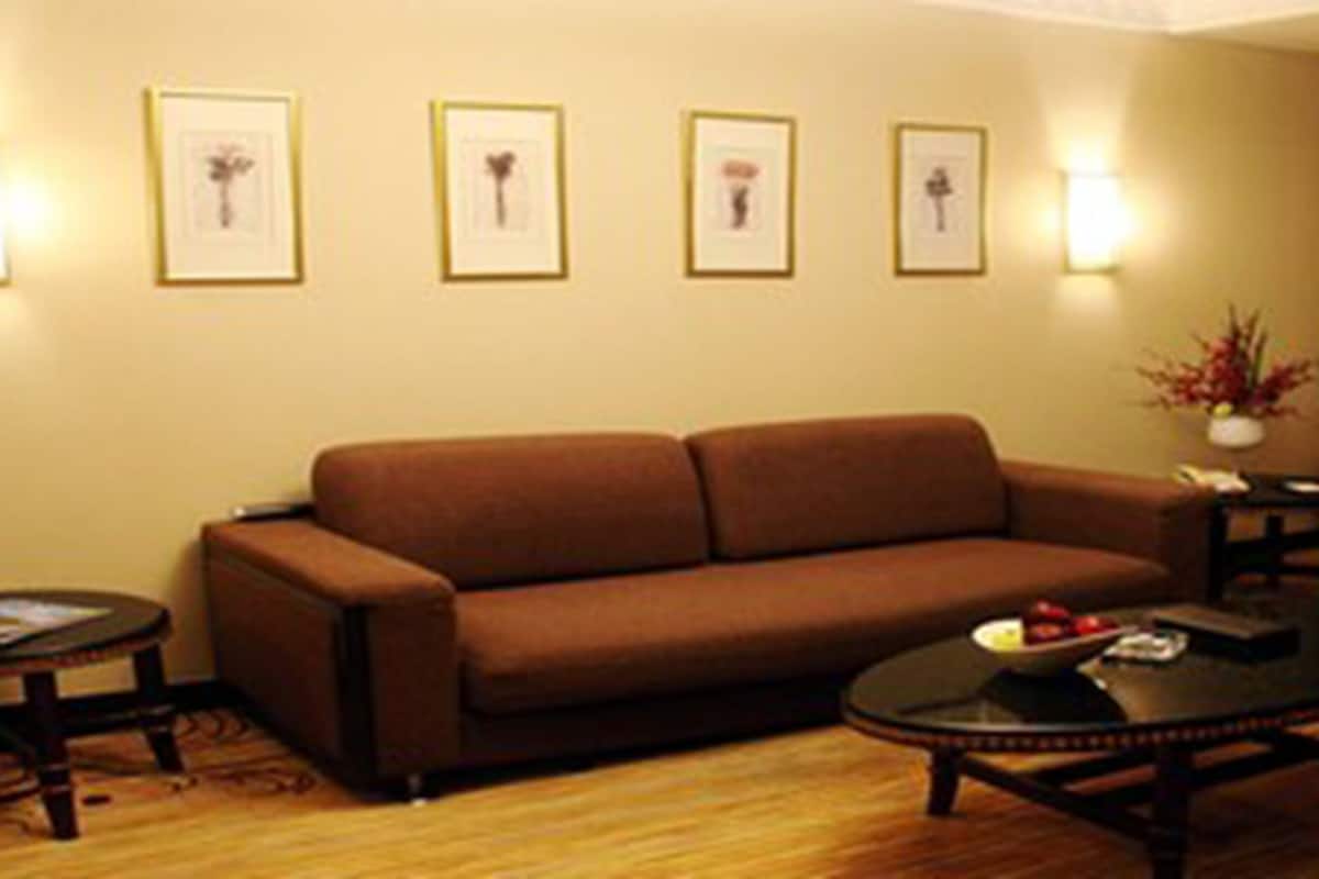 Un salón con un sofá marrón, una mesa de centro y dos mesitas auxiliares. Hay cuadros enmarcados en la pared y un jarrón con flores sobre una de las mesitas.