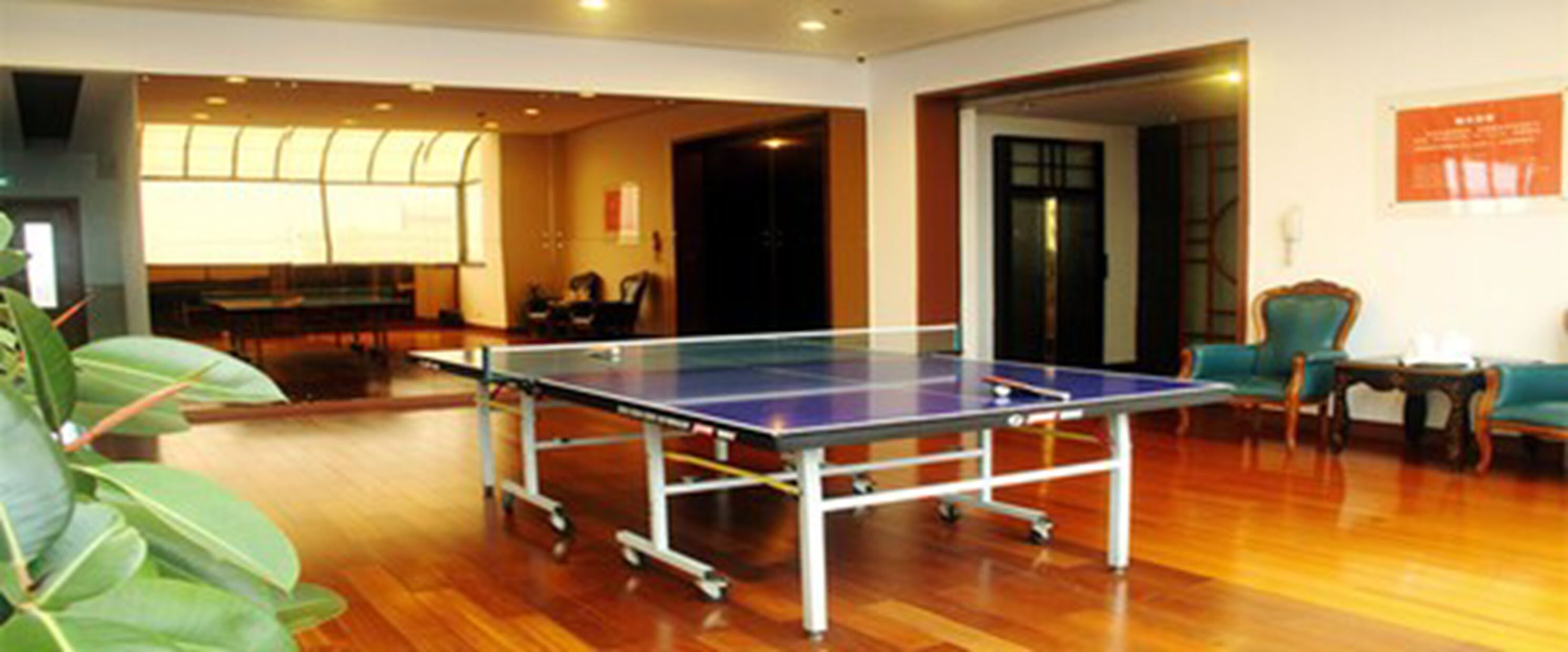 A ping pong table in a room with wooden flooring, a large window, and a door leading to another room.