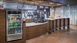 Un mostrador de desayuno autoservicio con dispensador de bebidas refrigeradas, una máquina de café y un panel informativo con el menú.