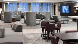 Un moderno vestíbulo de hotel con un área de estar que incluye sofás y sillones, un televisor de pantalla plana montado en la pared y un mostrador de recepción.