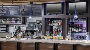 Zona de bar con una pizarra de menú, taburetes, estanterías con botellas y una máquina de café.