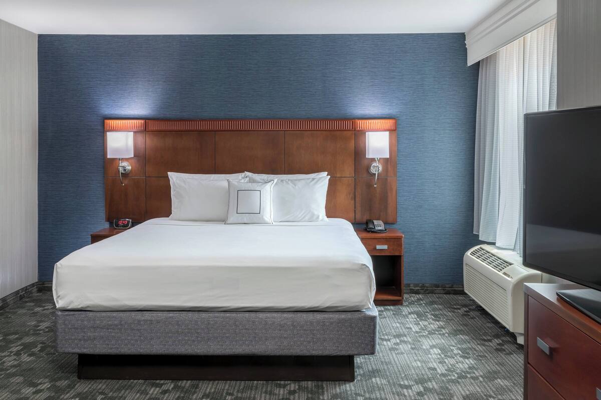 A hotel room with a large bed, two bedside tables with lamps, a TV, and a wall-mounted heater.