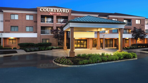 Un hotel Courtyard Marriott con entrada techada, fachada de ladrillo y zona ajardinada.