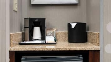 A kitchenette with a coffee maker, a trash can, and a refrigerator.
