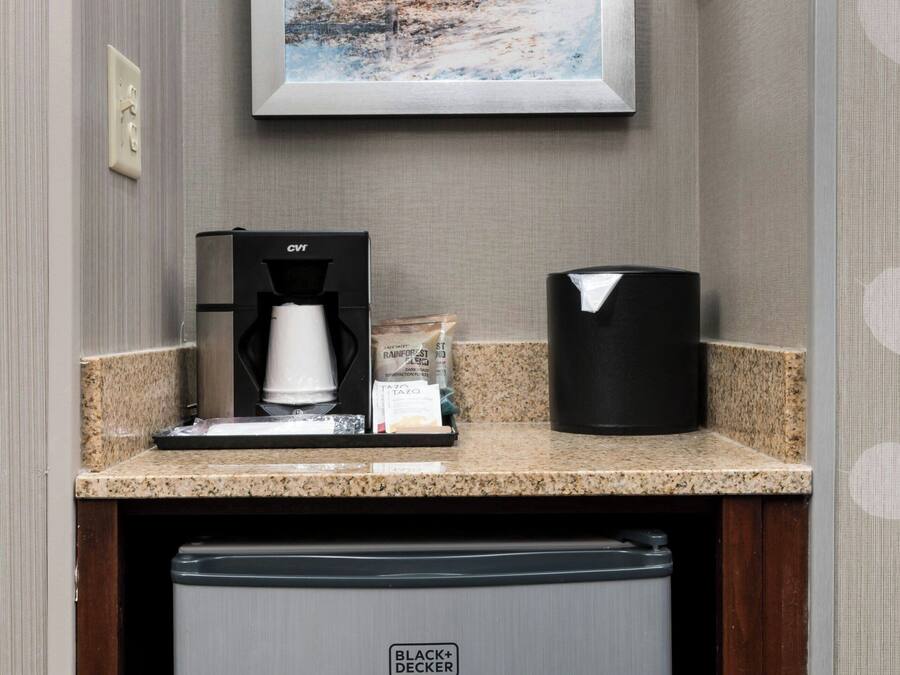 A kitchenette with a coffee maker, a trash can, and a refrigerator.