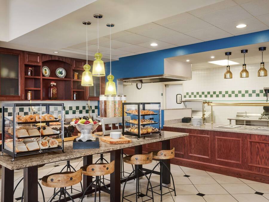 A kitchen with a central island, bar stools, and a variety of baked goods displayed on shelves.