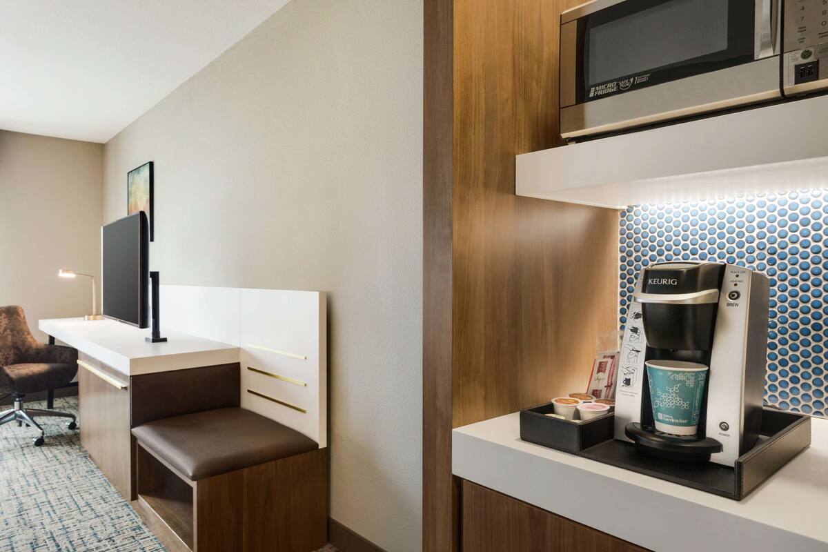 Ein kompaktes Hotelzimmer mit Küchenzeile, einem Flachbildfernseher, einer Sitzecke und einer Keurig-Kaffeemaschine.