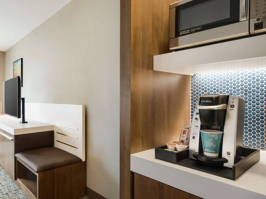 Habitación de hotel compacta con kitchenette, televisión de pantalla plana, zona de estar y cafetera Keurig.