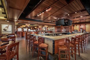 A restaurant with a bar area, wooden chairs, and a brick wall with a poster. - Hilton Garden Inn Dubuque Downtown (Dubuque)