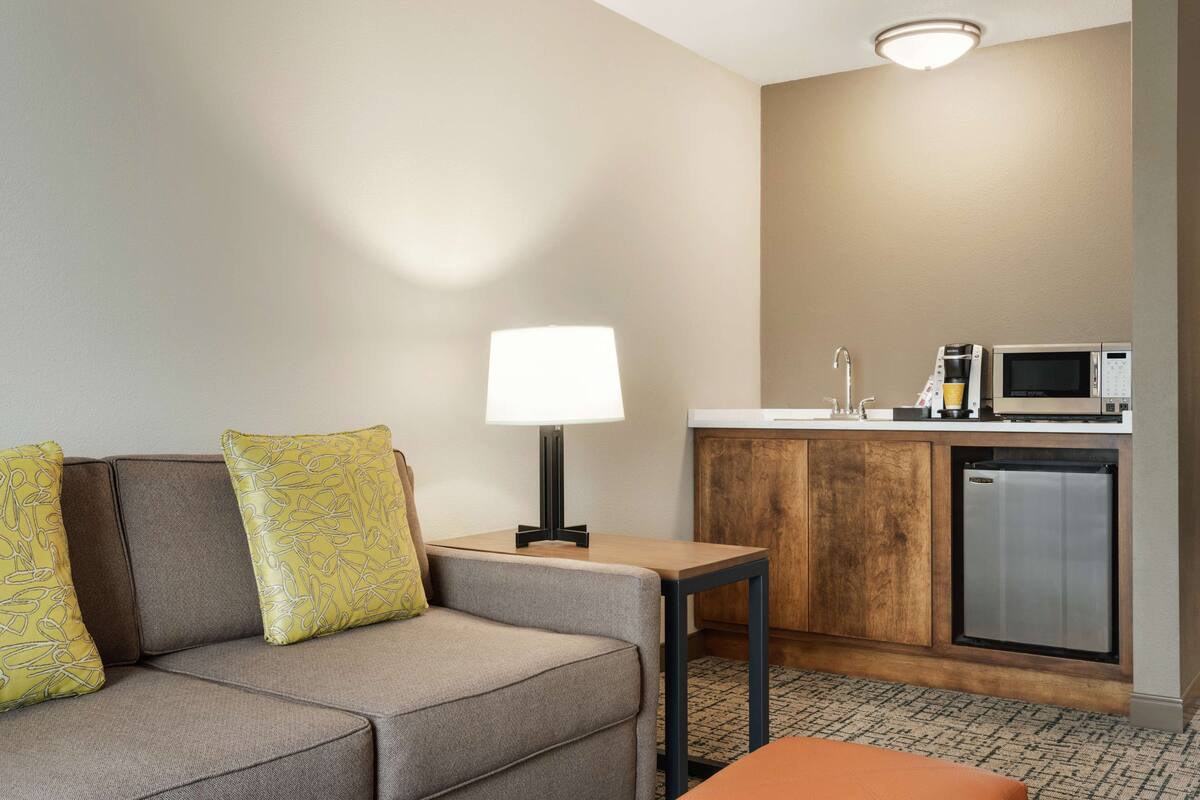 Ein Hotelzimmer mit einer Couch, einem kleinen Tisch mit Lampe, einer Küchenzeile inklusive Mikrowelle und Kühlschrank.