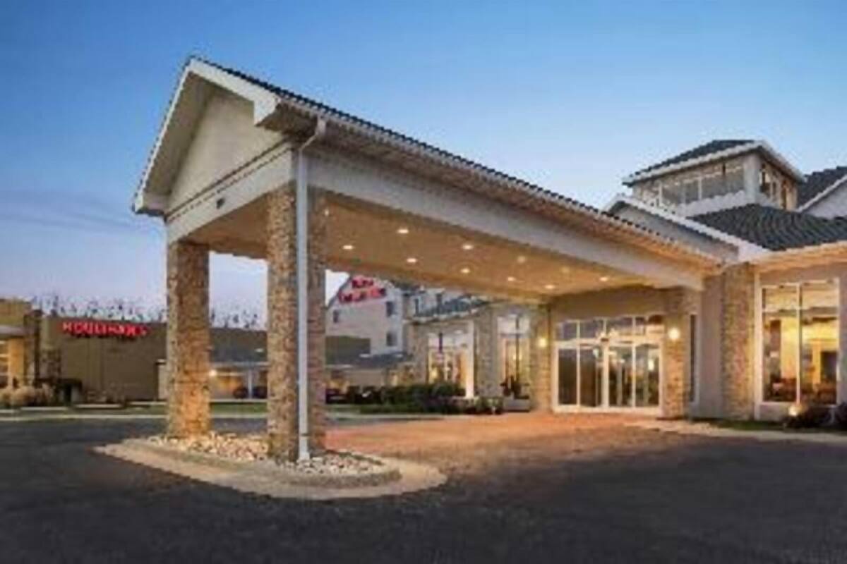 Ein Hotel mit Eingangsbereich, überdachtem Gang, Steinpfeilern und blauem Himmel.